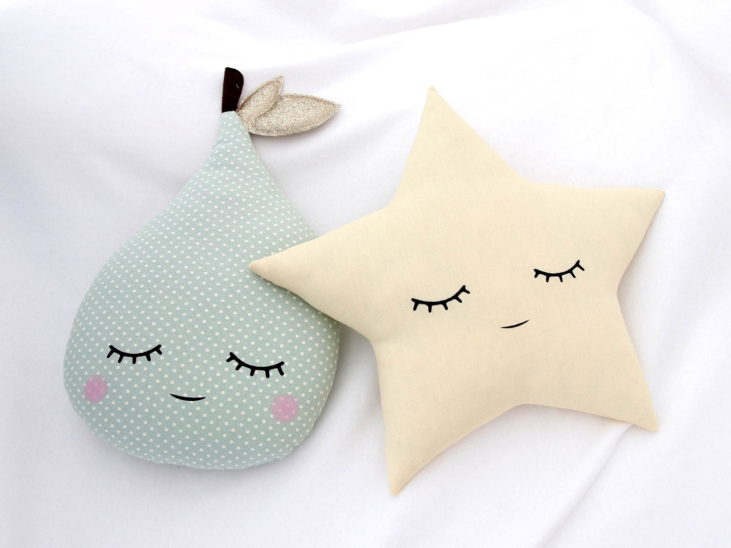 Decorative pillows shaped like a pear and a star with facial features on a white blanket