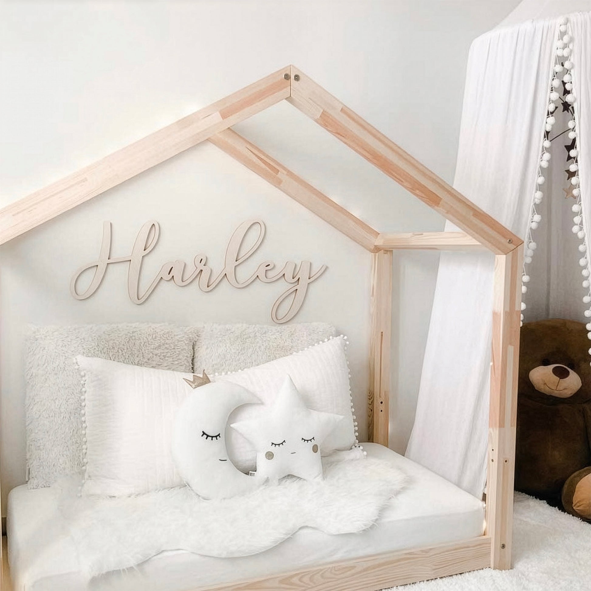 Children's bed with wooden frame and 'Harley' sign, featuring white bedding and decorative pillows.