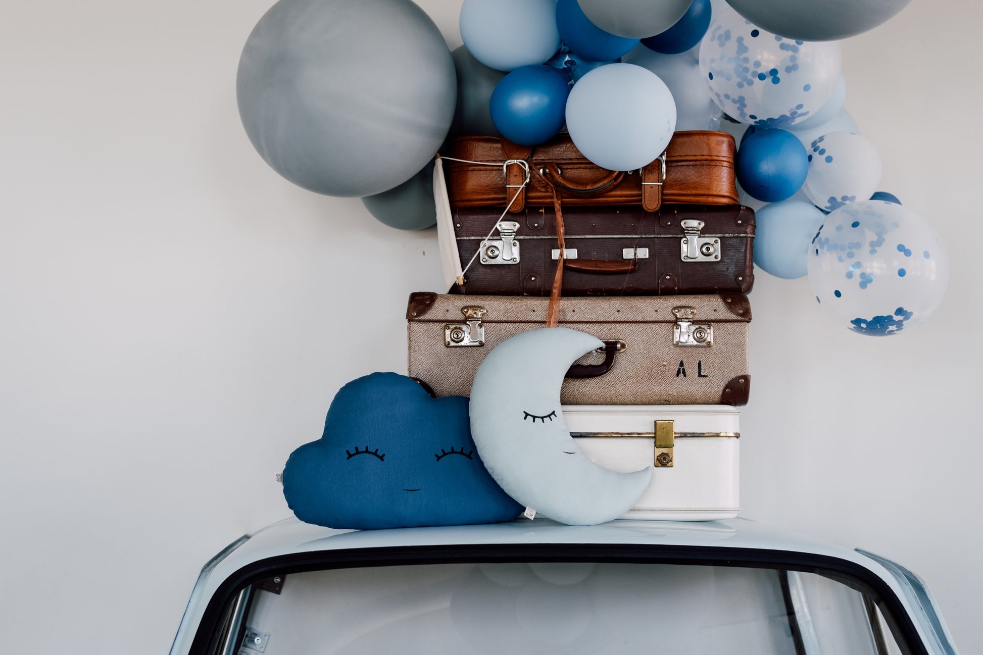 Decorative setup with balloons, suitcases, and throw pillows on a car roof.