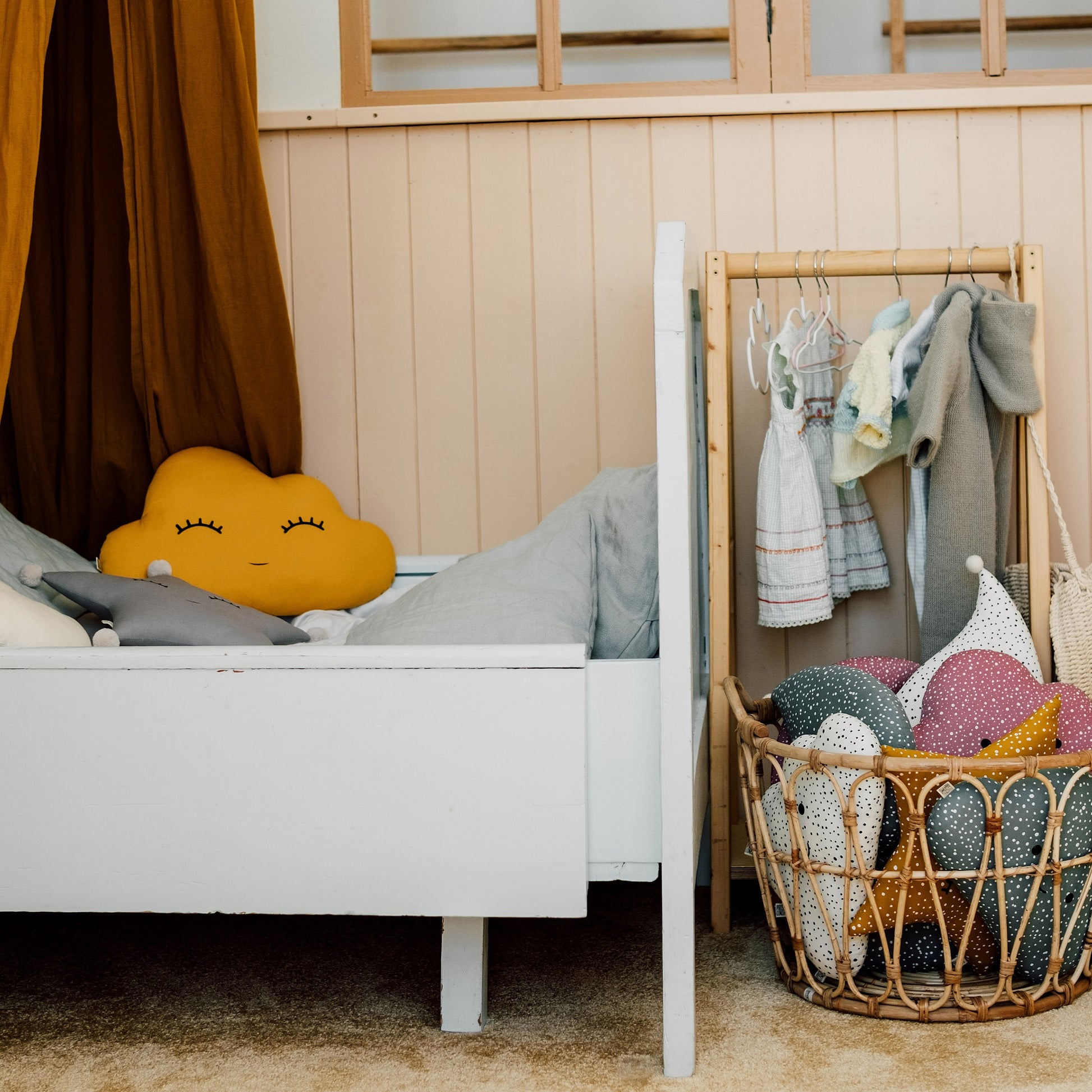 Children's bedroom with a bed, basket of toys, and clothes hanging on a rack.