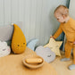 Baby in a mustard yellow outfit playing with colorful cushions in a nursery.