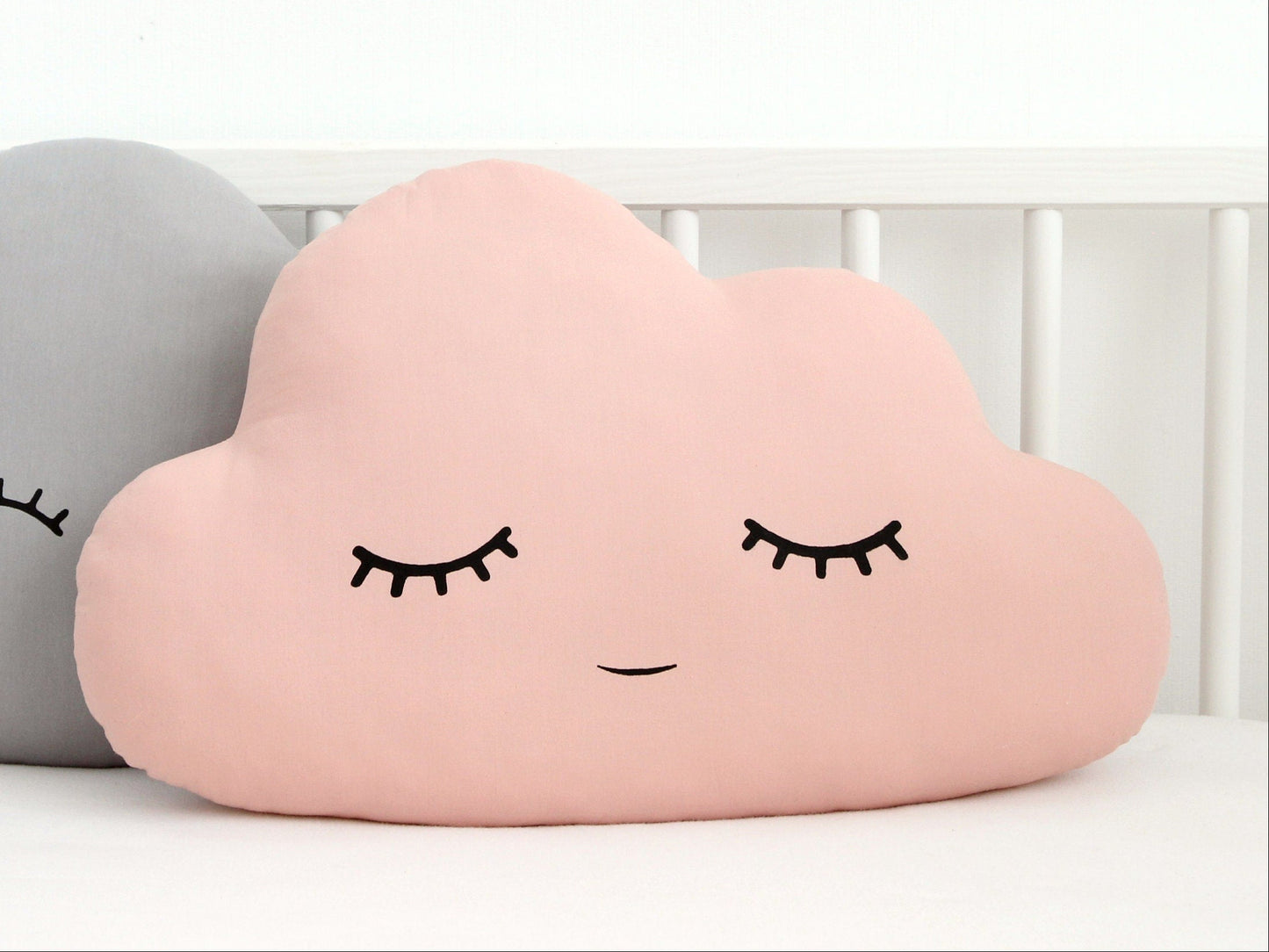 Pink cloud throw pillow, closed eyes and subtle smile – on bed beside gray version.