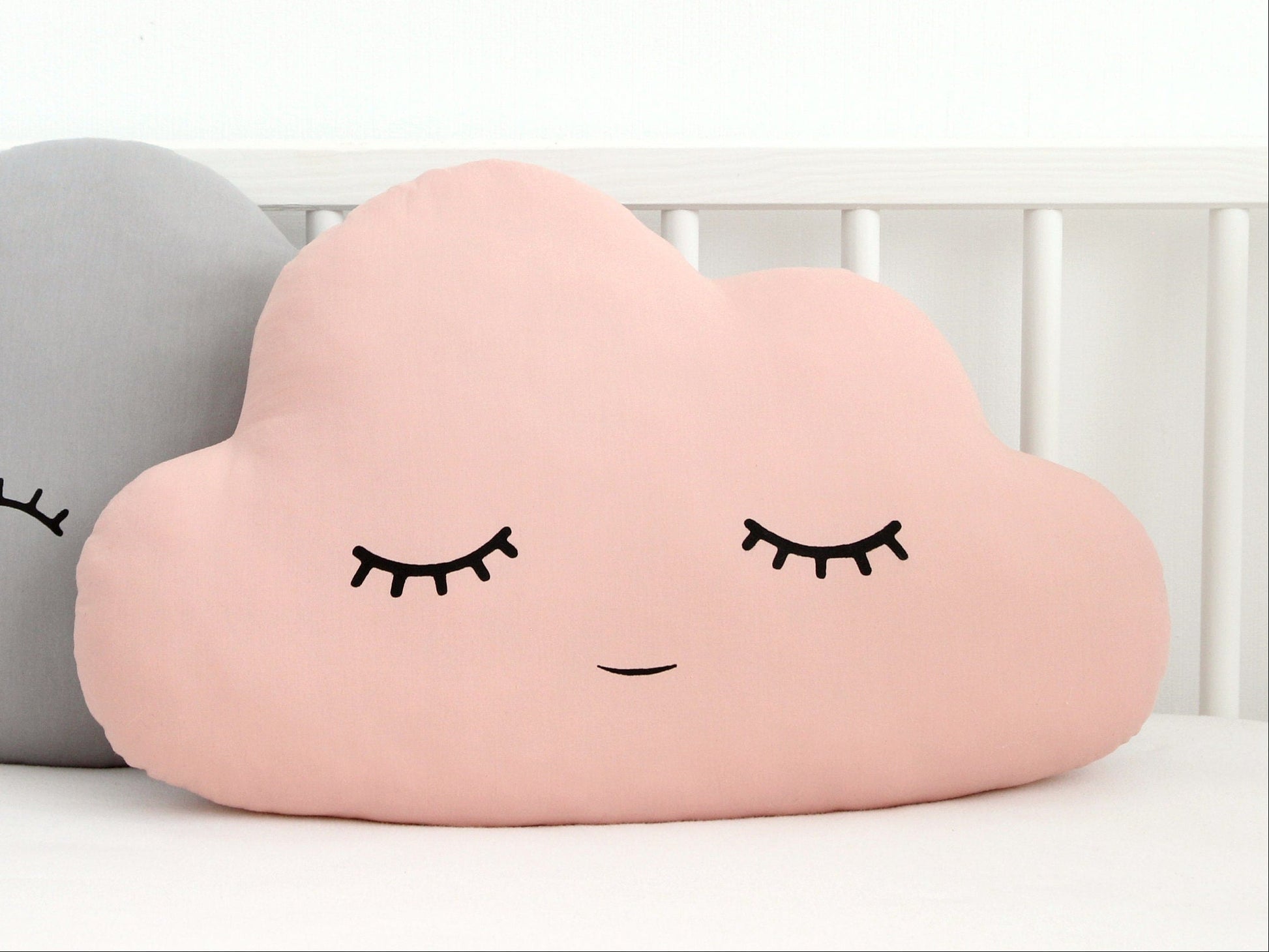 Pink cloud throw pillow, closed eyes and subtle smile – on bed beside gray version.