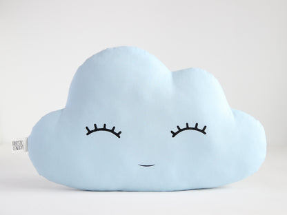 Light blue cloud-shaped throw pillow, closed eyes and small smile – plain white background.