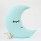 Mint crescent moon throw pillow, sleeping face and small polar bear toy at base – upright in nursery setting.