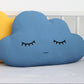 Petrol blue cloud-shaped throw pillow, closed eyes and gentle smile – on a childs bed or nursery decor.